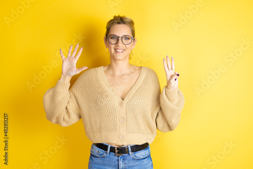 Young beautiful woman wearing casual sweater over isolated yellow background showing and pointing up with fingers number eight while smiling confident and happy