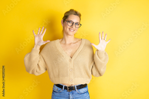 Young beautiful woman wearing casual sweater over isolated yellow background showing and pointing up with fingers number ten while smiling confident and happy