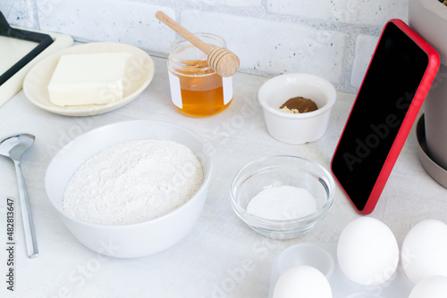 The concept of online lessons in the preparation of cookies. A smartphone in a red case and ingredients are on the table. Everything is ready for mixing future baking. Horizontal Orientation