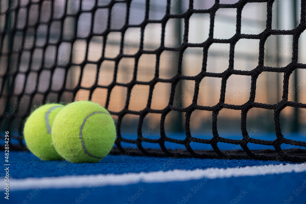 Selective focus. two paddle tennis balls by the net of a blue paddle tennis court at sunset