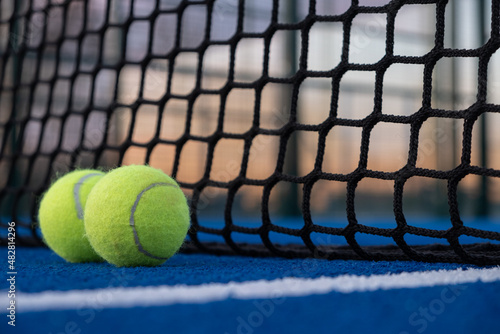 Selective focus. two paddle tennis balls by the net of a blue paddle tennis court at sunset © Vic