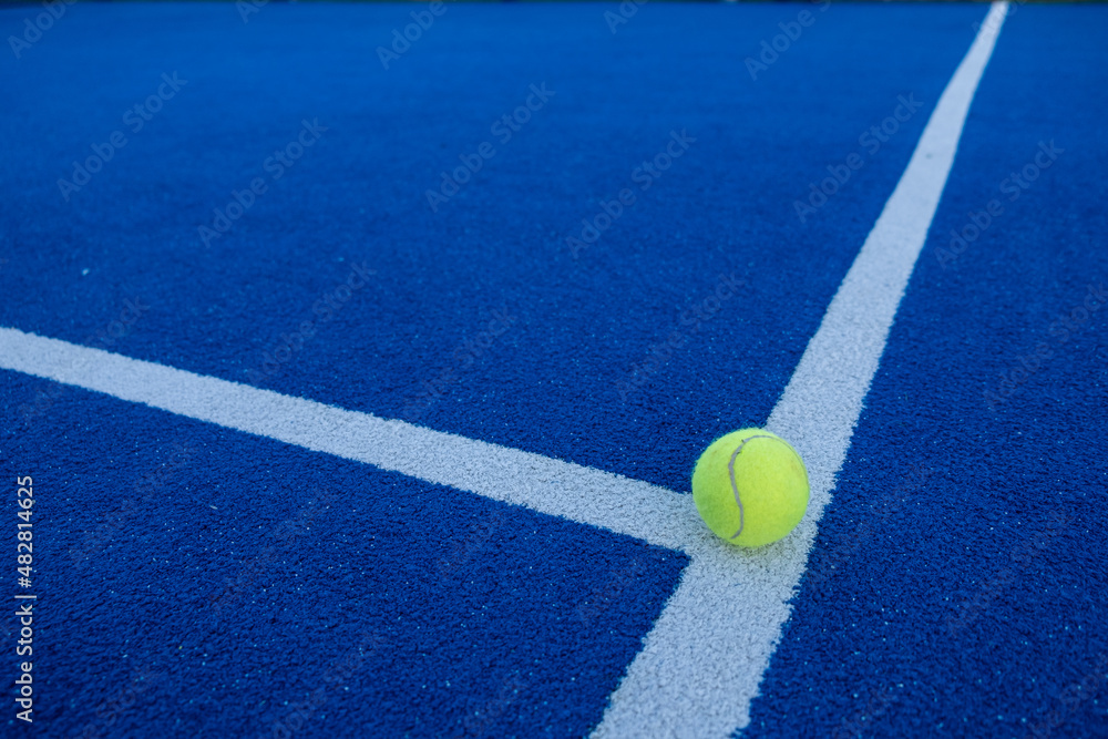 Paddle tennis ball on the line of a blue paddle tennis court.