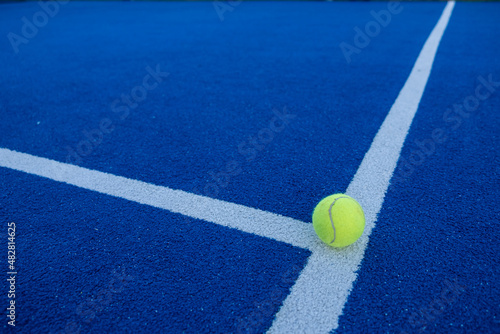 Paddle tennis ball on the line of a blue paddle tennis court. © Vic