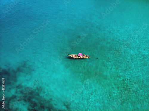 Fototapeta Naklejka Na Ścianę i Meble -  Aerial view of the wooden Thai boat with a pink parasol sailing the immensely clear sea, tourism; paradise concept.