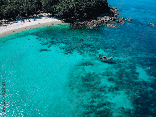 Drone view of the lagoon: narrow strip of the white sand, clear blue water and a small boat, green hills covered with tropical forest  paradise concept. © Semachkovsky 