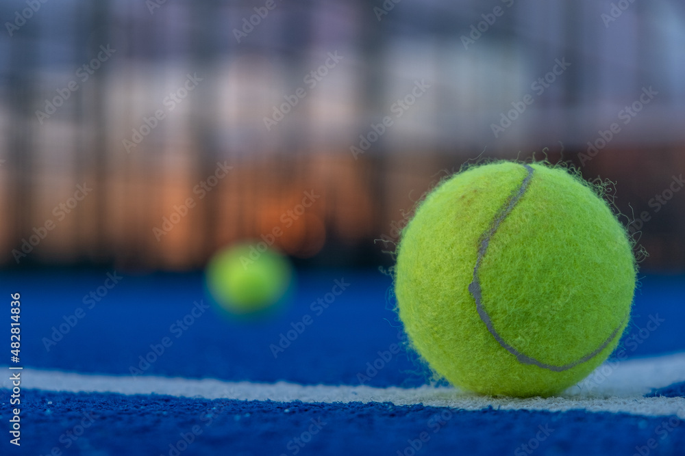 Selective focus. Paddle tennis ball in the foreground on a blue paddle tennis court at sunset.