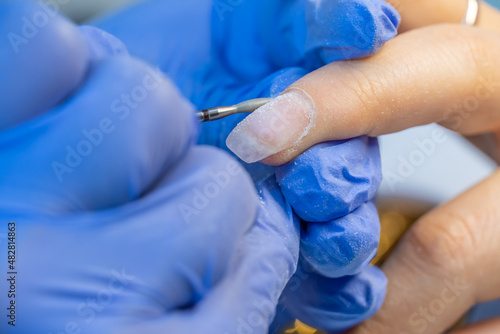 Close-up of the hands of a manicure master in blue gloves using an electric nail file to trim and remove cuticles in a beauty salon, macro. Hardware manicure