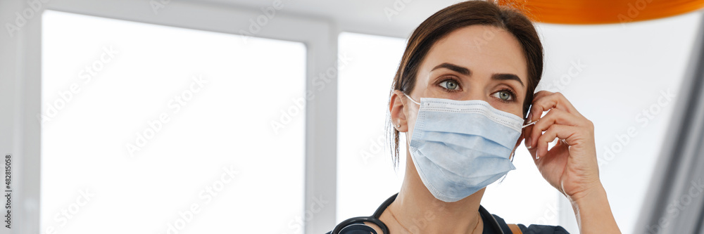 The woman doctor holding a tablet with papers and a phone in her hands while straightens a mask on her face The woman doctor holding a tablet with papers and a phone in her hands while straightens a mask on her face