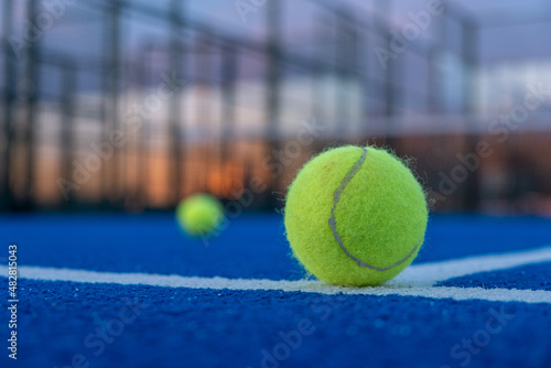Selective focus. Paddle tennis ball in the foreground on a blue paddle tennis court at sunset. © Vic