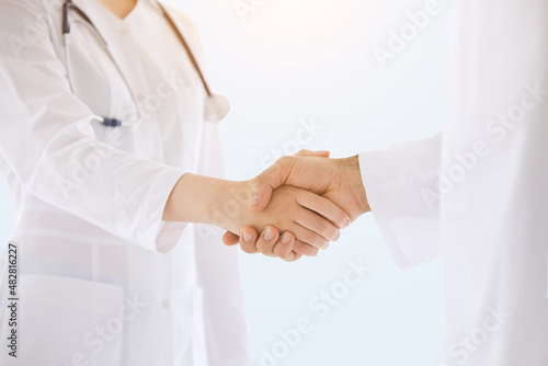 Healthcare, medicine concept: Doctors in lab coats greeting each other with handshake isolated over grey color background