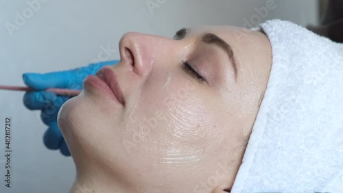 A young beautiful girl lies on the table at the beautician, hands in blue gloves apply a moisturizing cream, a mask with a brush   