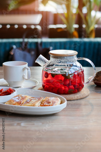Raspberry tea in a teapot and pancakes for breakfast in a cafe.