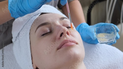 A young beautiful girl lies on the table at the beautician, hands in blue gloves apply a moisturizing cream, a mask with a brush   
