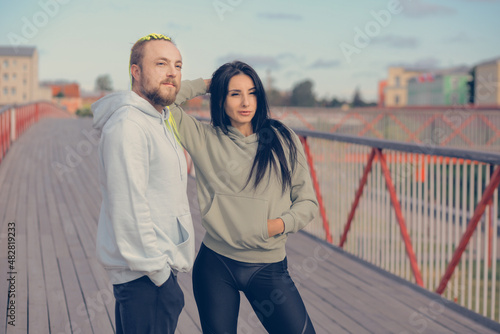 A man and a woman in sweatshirts stand on a bridge getting ready for their morning run