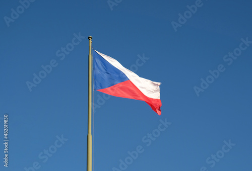 National flag of the Czech Republic, tricolor of red, white and blue. The Czech flag on a flagpole flutters in the wind against a blue sky.