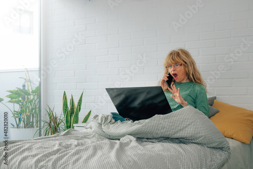 woman at home with computer and mobile phone surprised