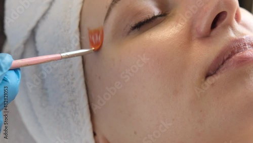 A young beautiful girl lies on the table at the beautician, hands in blue gloves apply a moisturizing cream, a mask with a brush   