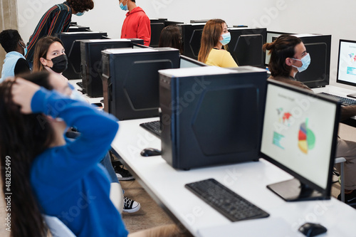 Multiracial young students using computers during coronavirus outbreak inside technology classroom - Focus on right girl face