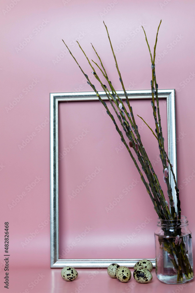 A willow stands in a jar of water next to a frame and an egg on a pink background A willow stands in a jar of water next to a frame and an egg on a pink background