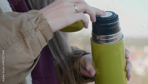 a tourist girl opens the lid of a green thermos to drink hot tea in nature. unscrew the lid of the thermos with a drink. quenching thirst on a hike.