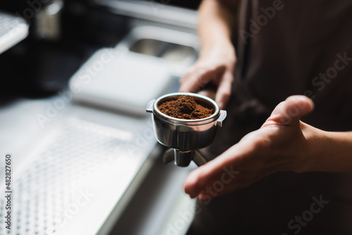 Cropped view of blurred barista holding portafilter with coffee in cafe.