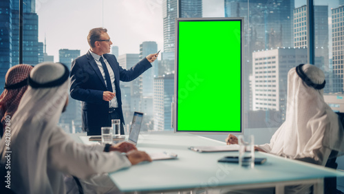 International Manager Holds Meeting Presentation for Saudi Business Partners. Specialist Uses Whiteboard with Vertical Green Screen Mock Up Display. Saudi, Emirati, Arab Office Concept.
