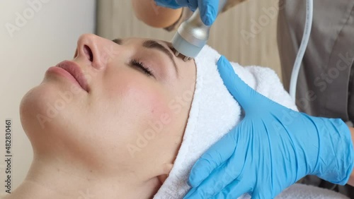 Young woman lying on cosmetologist's table during rejuvenation procedure. Cosmetologist take care about neck and face skin youthfull and wellness. Hardware face cleaning procedure  