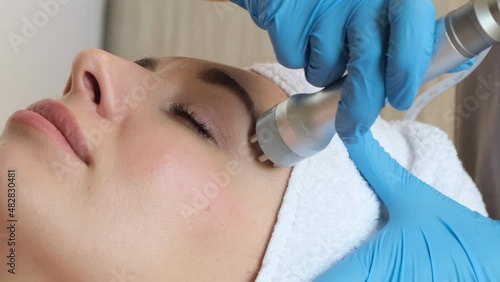 Young woman lying on cosmetologist's table during rejuvenation procedure. Cosmetologist take care about neck and face skin youthfull and wellness. Hardware face cleaning procedure  