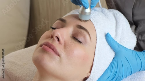 Young woman lying on cosmetologist's table during rejuvenation procedure. Cosmetologist take care about neck and face skin youthfull and wellness. Hardware face cleaning procedure  