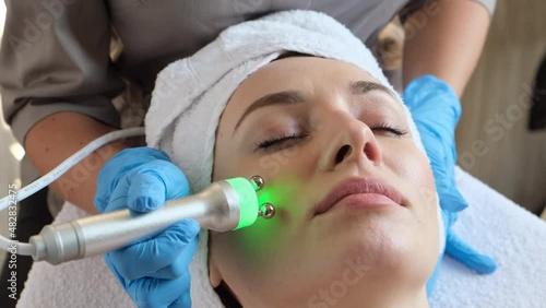 Young woman lying on cosmetologist's table during rejuvenation procedure. Cosmetologist take care about neck and face skin youthfull and wellness. Hardware face cleaning procedure  