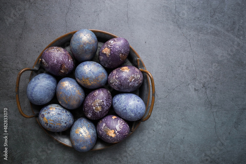 Easter card with a copy of the place for the text. Purple, blue and golden eggs in an iron plate on a dark background. The purple hue trend of 2022 is veryperi. Natural dye karkade tea. Top view.