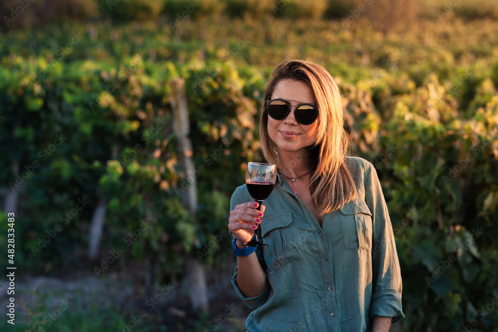 Beautiful girl holding wine glass in nature near vineyard field
