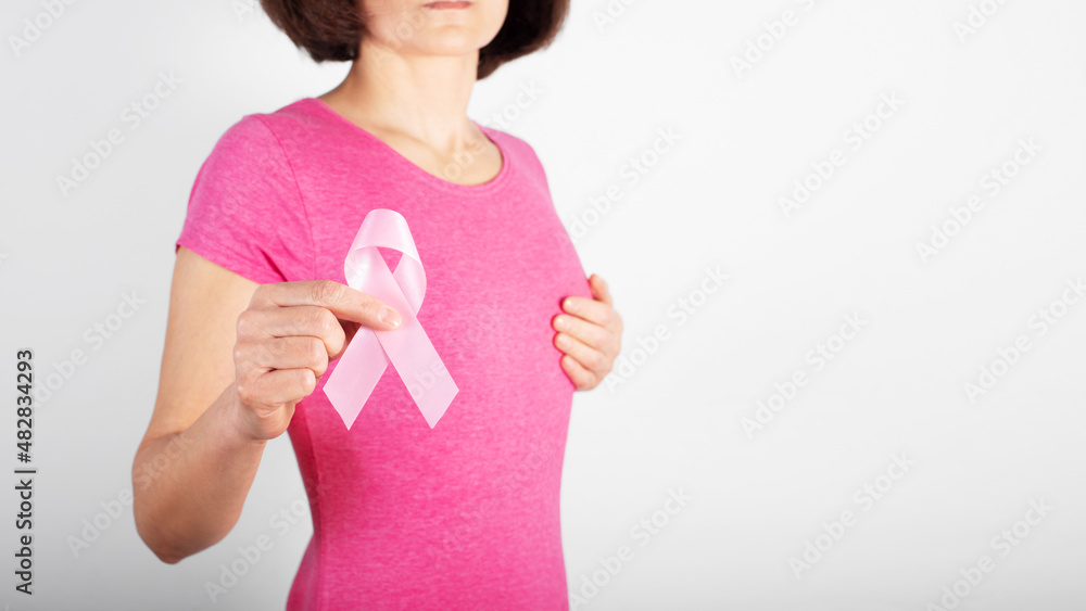Middle aged caucasian woman shows pink ribbon as symbol of breast cancer awareness