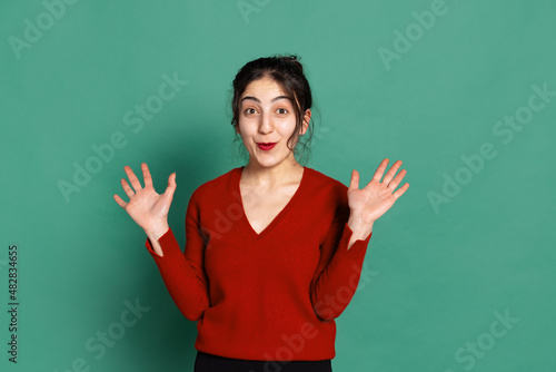 Young surprised arabian girl in red pullover isolated on green background. Concept of emotions, facial expressions