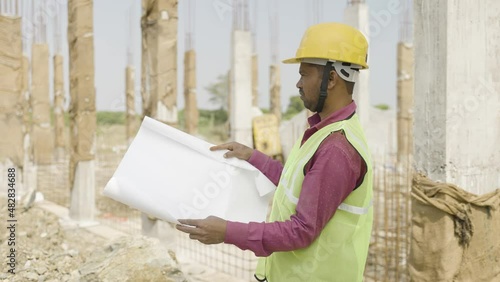 young indian engineer or supervioser inspecting construction plan at workplace - concept of skilled labour,daily wager lifestyle and construcation service.