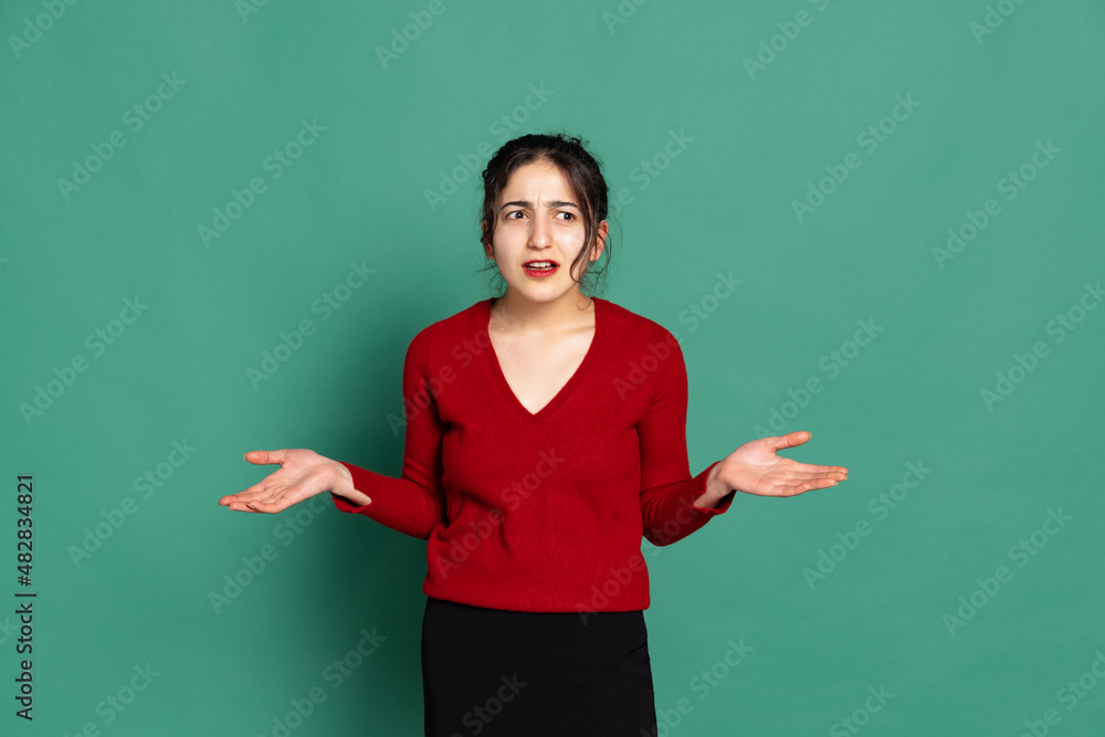 Annoyed young pretty girl in red pullover isolated on green background. Concept of emotions, facial expressions