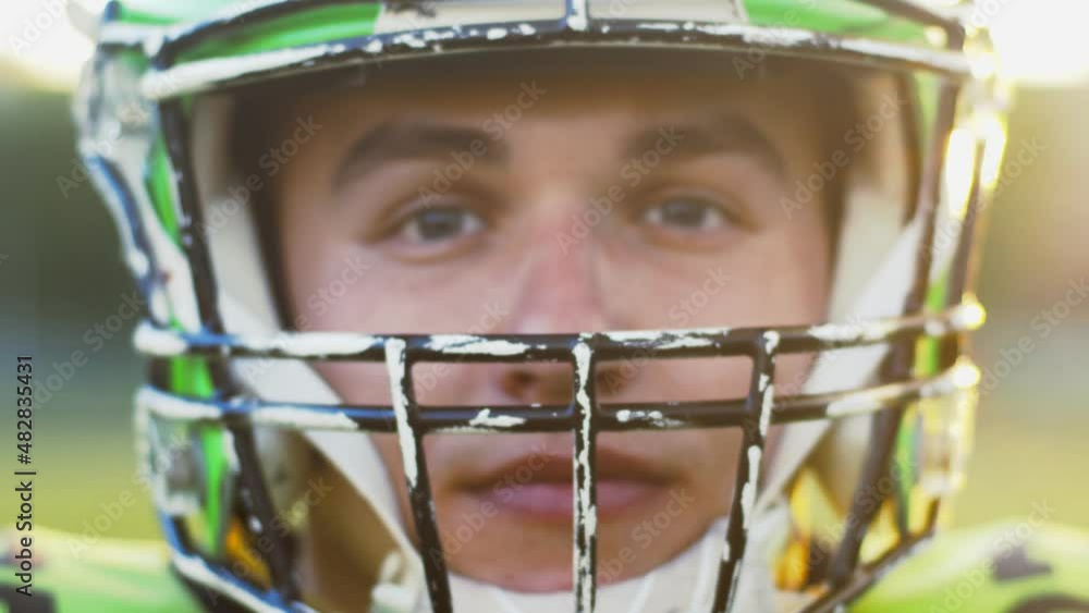 Close up portrait view of the American football player in a helmet standing on a field with golden sunset at the background. Sport concept Close up portrait view of the American football player in a helmet standing on a field with golden sunset at the background. Sport concept