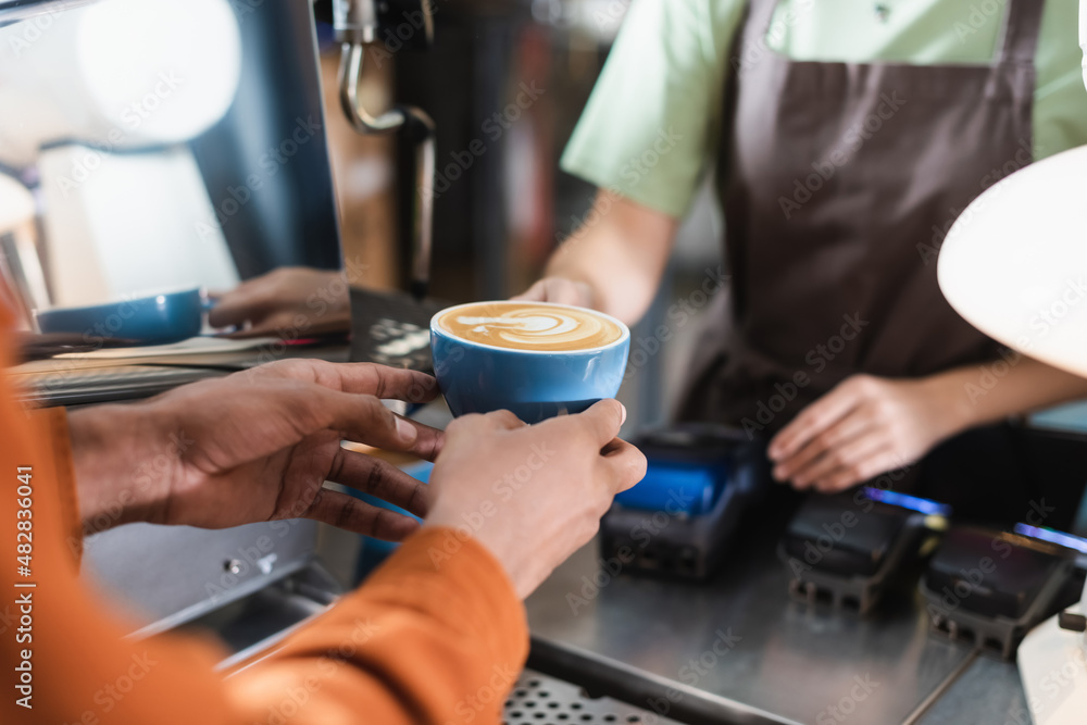 Cropped view of african american man holding coffee near blurred barista in cafe. Cropped view of african american man holding coffee near blurred barista in cafe.