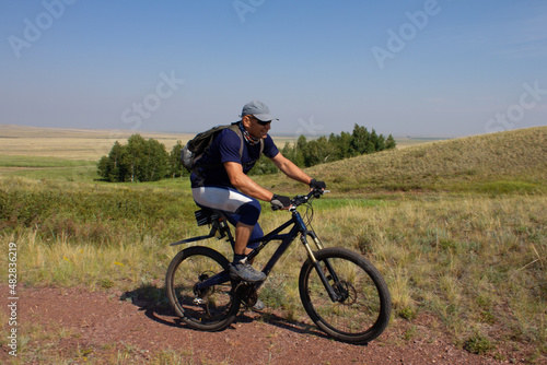 Smiling man with the backpack travelling by bicycle along the steppe road. Active leisure concept.