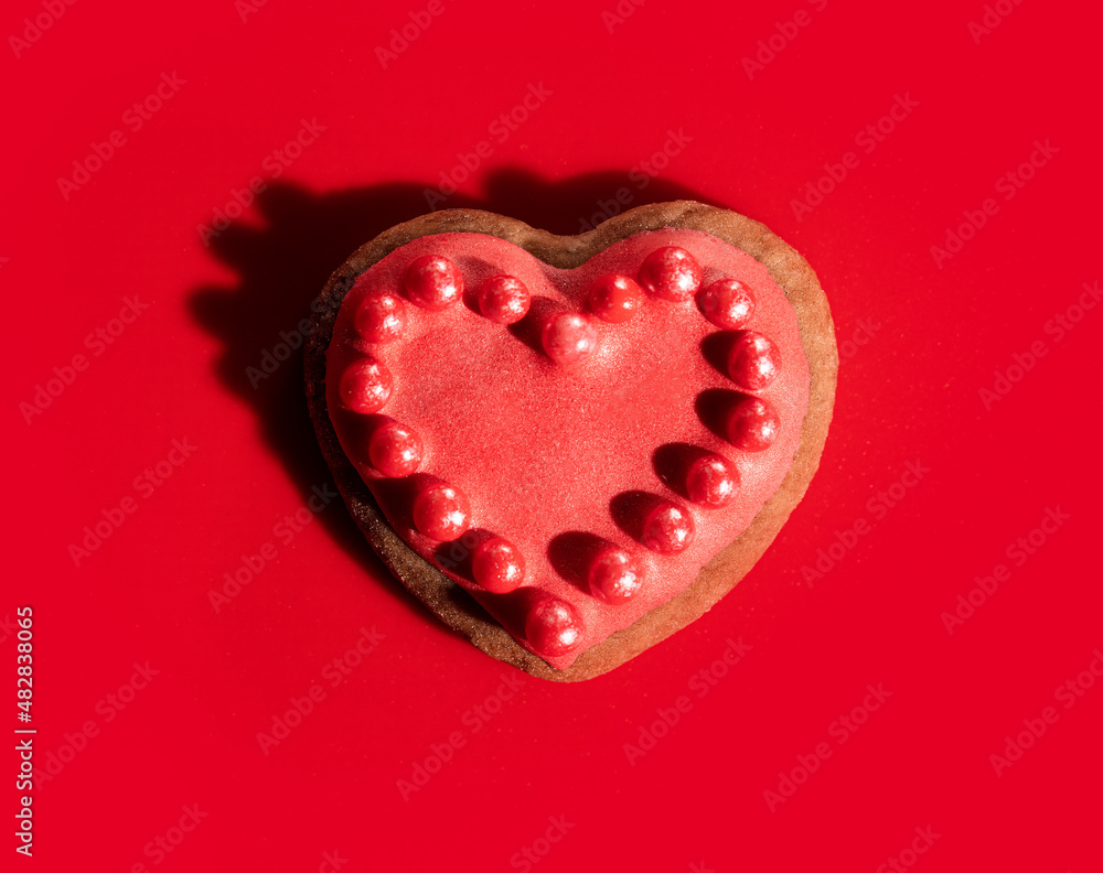 Top macro view of cookie in shape of heart decorated by pink icing and bead sprinkles on solid red background Top macro view of cookie in shape of heart decorated by pink icing and bead sprinkles on solid red background