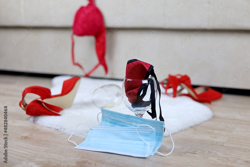 Two medical masks, wine glass with female thong panties, red bra and