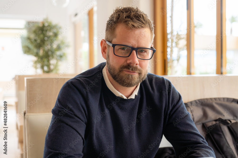 Portrait of a bearded man in glasses looking at camera sitting in café or coffeeshop. Portrait of a bearded man in glasses looking at camera sitting in café or coffeeshop.