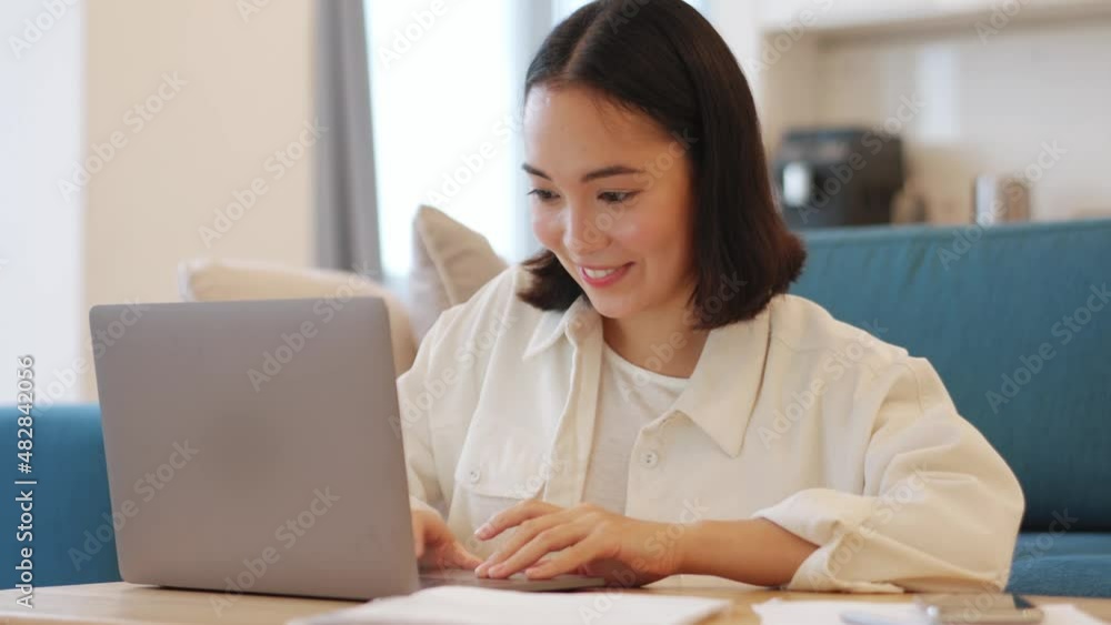 Cheerful Asian woman working on laptop at home Cheerful Asian woman working on laptop at home