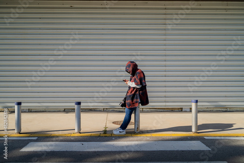 Chica mirando smartphone mientras espera apoyada en una barra