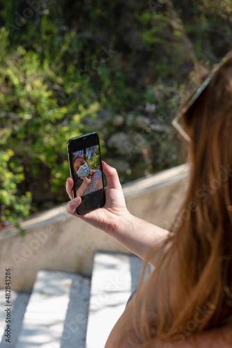 Unrecognizable woman with facial mask uses smart phone to take selfie.