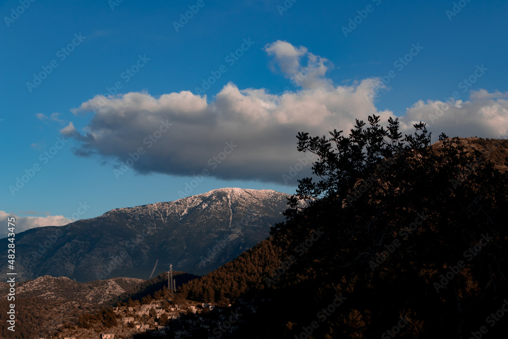 There is snow top of the mountain. Big gray cloud on blue sky.it's about to rain. Fethiye Kayaköy, Turkey.