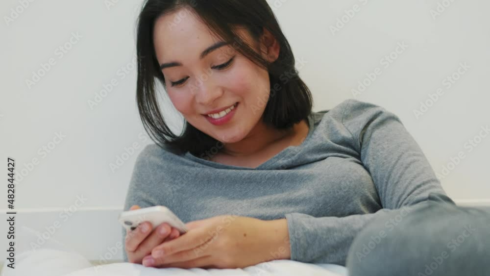 Laughing Asian woman texting by phone at home Laughing Asian woman texting by phone at home