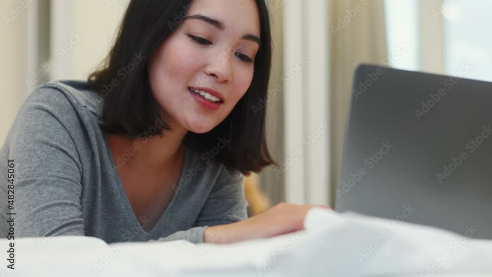 Smiling Asian woman typing by laptop on the bed at home Smiling Asian woman typing by laptop on the bed at home