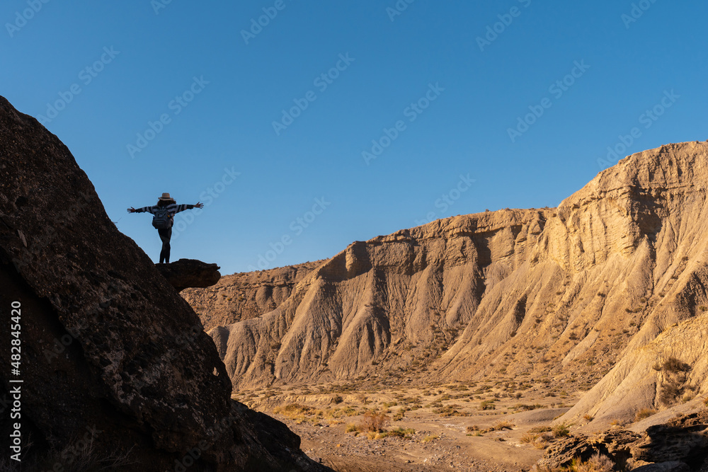 Silhouette of a free young woman with open arms climbing a rock in the desert of Tabernas, province of Almería, Andalusia. A trek in the Rambla Las Salinas