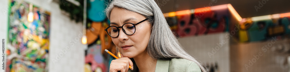 Mature grey thinking woman working with planner in cafe indoors Mature grey thinking woman working with planner in cafe indoors